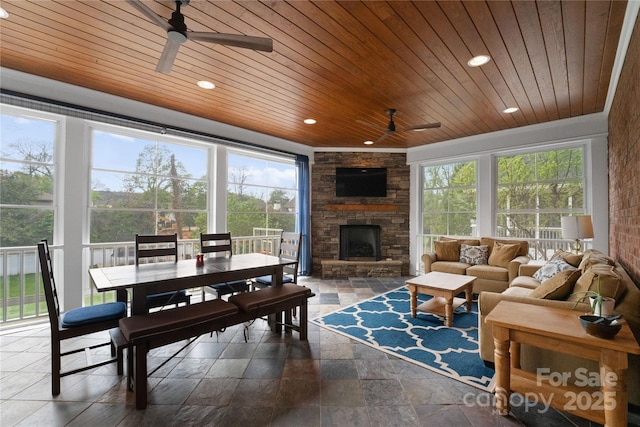 sunroom / solarium with wooden ceiling, ceiling fan, a wealth of natural light, and a stone fireplace