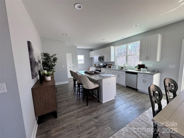 kitchen featuring dark wood-type flooring, sink, appliances with stainless steel finishes, a kitchen island, and white cabinets