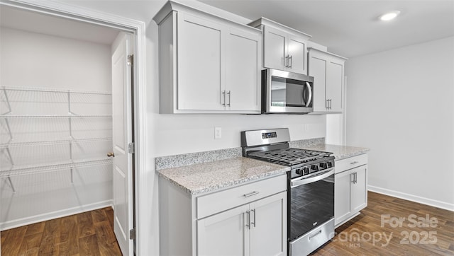 kitchen featuring dark wood-type flooring, stainless steel appliances, light stone countertops, and white cabinets