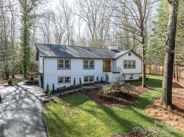 raised ranch featuring driveway, a chimney, fence, and a front yard