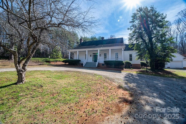 view of front of property with a porch, a front lawn, a chimney, and dirt driveway