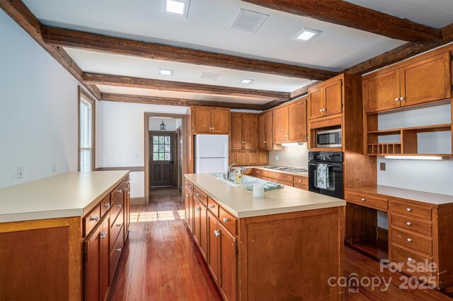 kitchen featuring brown cabinets, a center island with sink, stainless steel appliances, and light countertops