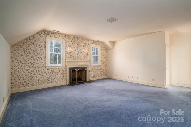 unfurnished living room featuring lofted ceiling, carpet floors, a fireplace with flush hearth, baseboards, and wallpapered walls