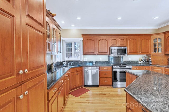 119 Era St, Troutman, NC 28166 - kitchen with stainless steel appliances, brown cabinetry, crown molding, dark stone counters, and light wood-type flooring