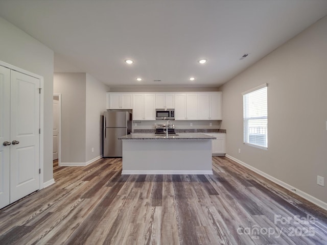 kitchen with a center island with sink, sink, dark wood-type flooring, appliances with stainless steel finishes, and white cabinets