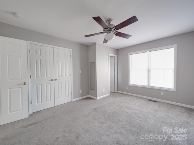 unfurnished bedroom with a closet, visible vents, a ceiling fan, light carpet, and baseboards