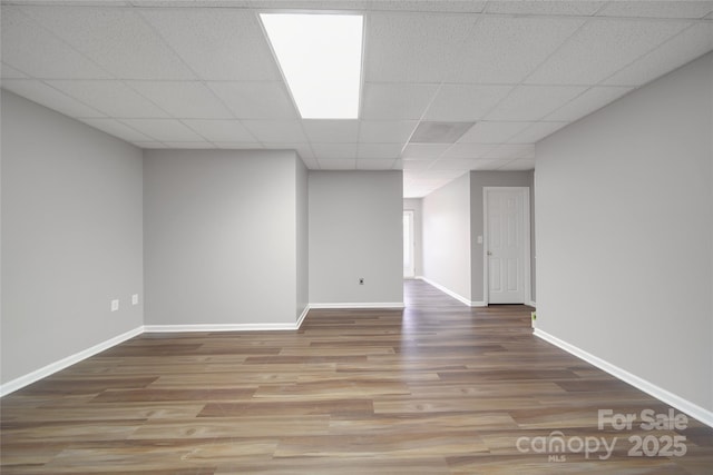 below grade area with baseboards, a drop ceiling, and wood finished floors