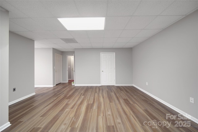 below grade area featuring a paneled ceiling, baseboards, and wood finished floors