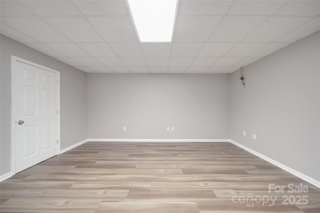 finished below grade area with a paneled ceiling, light wood-style flooring, and baseboards