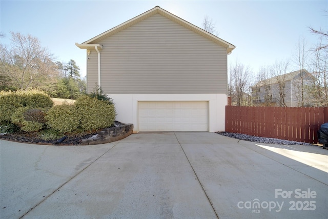 view of side of home featuring a garage, concrete driveway, fence, and stucco siding