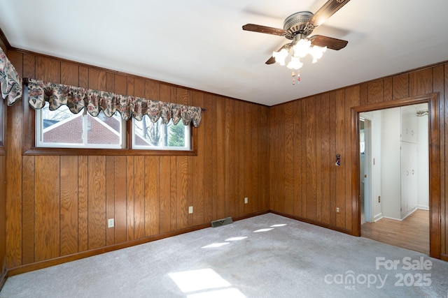 carpeted spare room featuring wood walls and ceiling fan