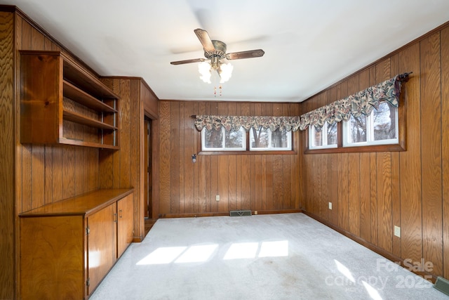 spare room featuring ceiling fan, light colored carpet, and wooden walls