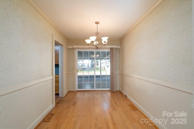 unfurnished dining area featuring light hardwood / wood-style flooring, crown molding, and a notable chandelier