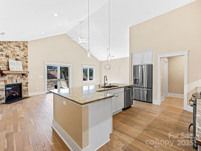 kitchen with sink, white cabinetry, a center island with sink, stainless steel appliances, and light stone countertops