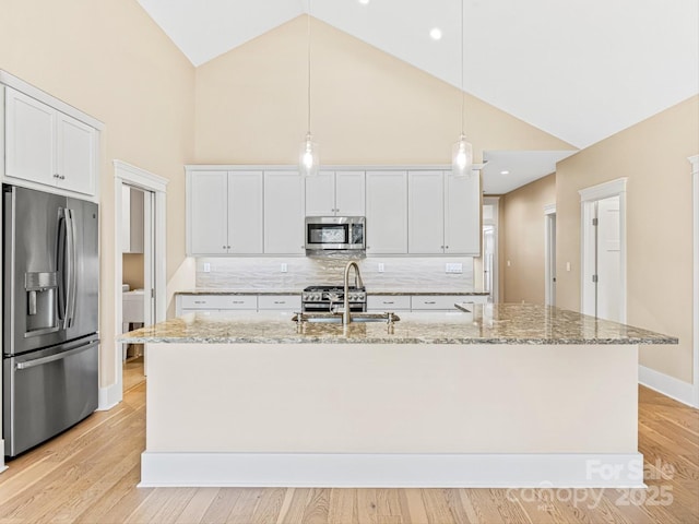 kitchen with appliances with stainless steel finishes, decorative light fixtures, sink, white cabinets, and a kitchen island with sink