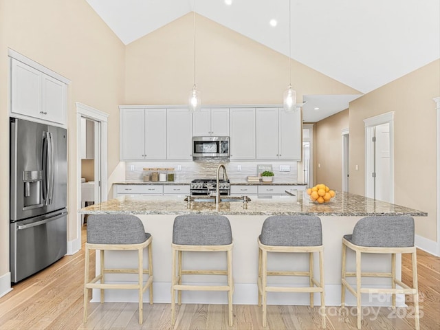 kitchen featuring white cabinetry, sink, light stone counters, stainless steel appliances, and a center island with sink