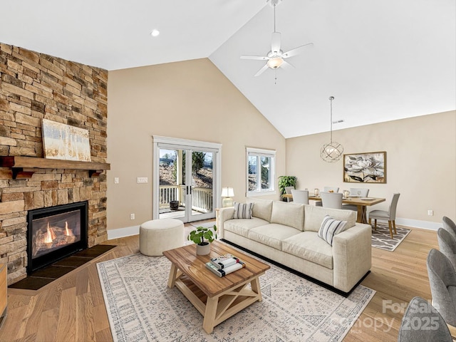 living room featuring ceiling fan, a stone fireplace, high vaulted ceiling, and light hardwood / wood-style flooring