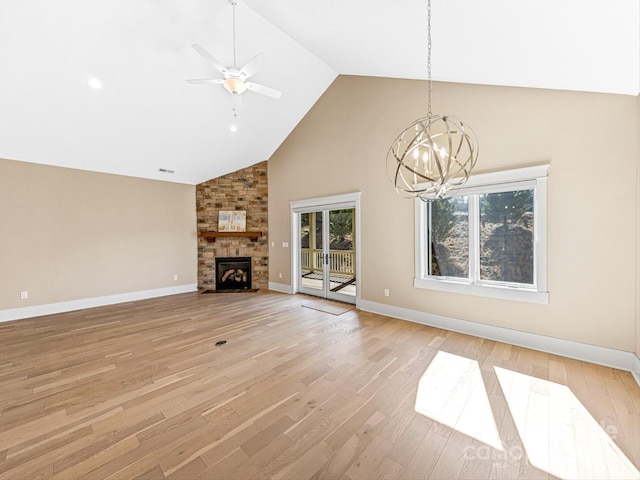 unfurnished living room featuring ceiling fan with notable chandelier, high vaulted ceiling, a large fireplace, and light wood-type flooring