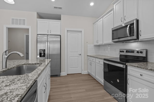 kitchen featuring appliances with stainless steel finishes, a sink, light stone countertops, and white cabinets