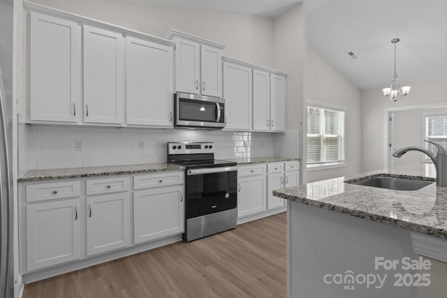 kitchen with hanging light fixtures, light stone countertops, stainless steel appliances, white cabinetry, and a sink