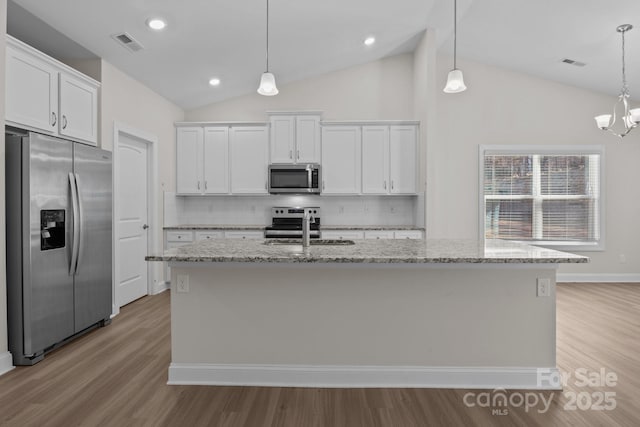 kitchen featuring visible vents, white cabinets, an island with sink, decorative light fixtures, and stainless steel appliances