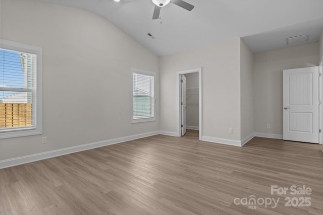 unfurnished bedroom with baseboards, visible vents, a spacious closet, vaulted ceiling, and light wood-type flooring