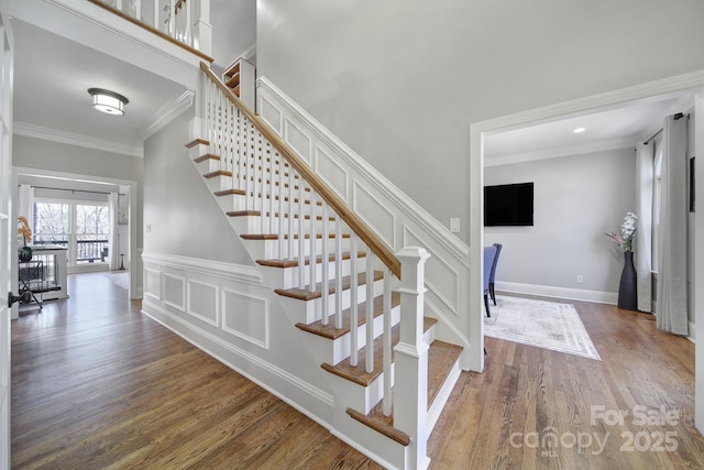 stairway featuring baseboards, a wainscoted wall, ornamental molding, wood finished floors, and a decorative wall