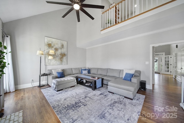 living area with baseboards, wood finished floors, and a towering ceiling