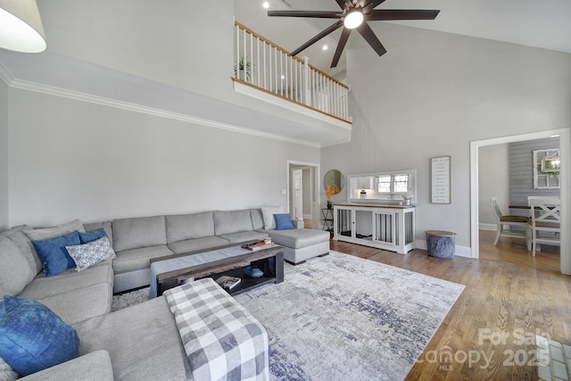 living area with wood finished floors, baseboards, high vaulted ceiling, ceiling fan, and crown molding