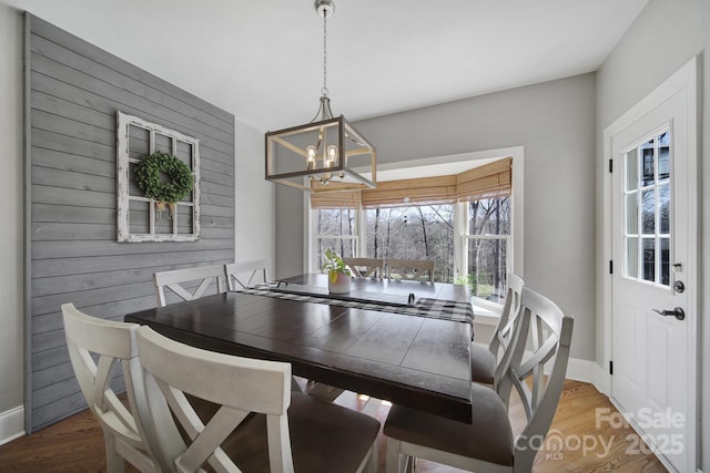 dining room featuring wood finished floors, baseboards, wood walls, and a chandelier