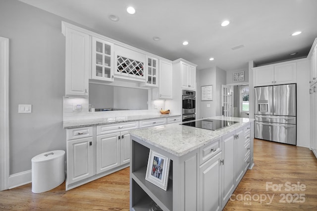 kitchen with a kitchen island, white cabinetry, appliances with stainless steel finishes, light wood finished floors, and glass insert cabinets