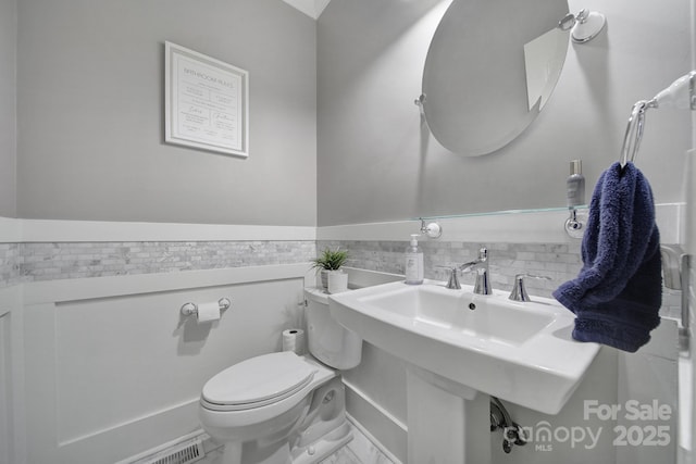 bathroom with a wainscoted wall, toilet, and a sink