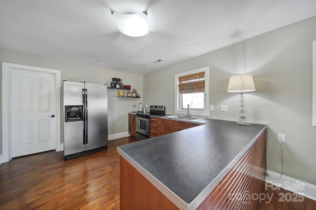 kitchen with dark countertops, a peninsula, dark wood-style floors, stainless steel appliances, and a sink