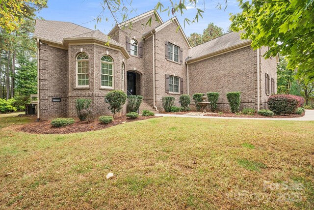 traditional-style house featuring a front yard, central AC, and brick siding