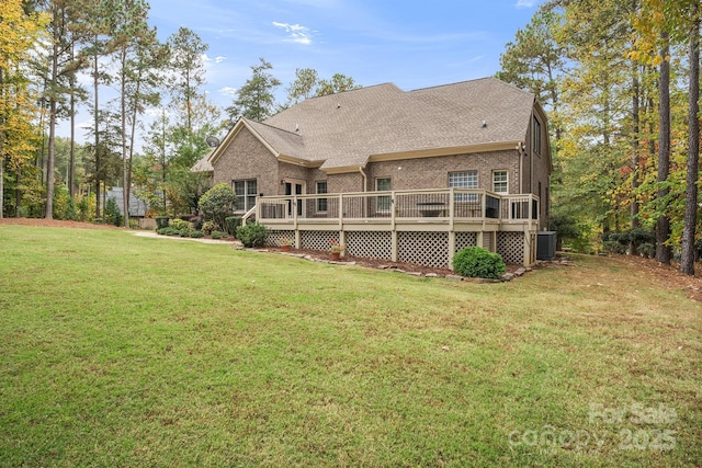 rear view of house featuring a deck, cooling unit, brick siding, roof with shingles, and a lawn