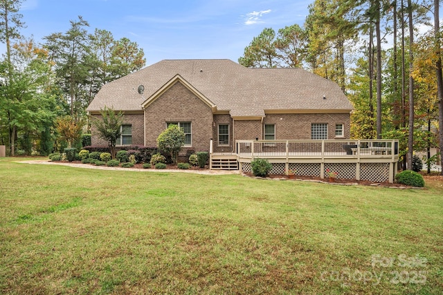 back of property featuring roof with shingles, brick siding, a lawn, and a wooden deck