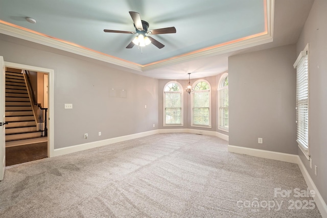 carpeted empty room featuring stairs, a tray ceiling, ceiling fan with notable chandelier, and baseboards