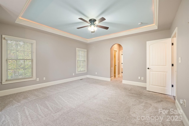 unfurnished room featuring a tray ceiling, light colored carpet, and arched walkways