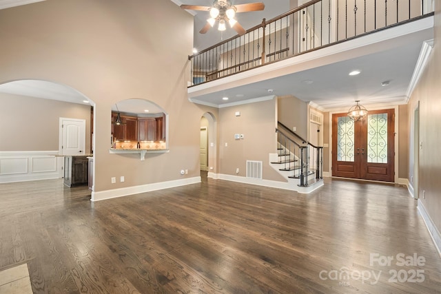 unfurnished living room with arched walkways, a high ceiling, visible vents, ornamental molding, and dark wood-style floors