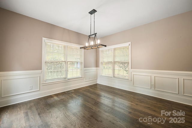 unfurnished dining area with dark wood-style floors, visible vents, a notable chandelier, and a wainscoted wall