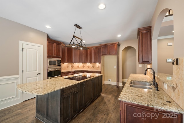 kitchen with arched walkways, stainless steel appliances, a sink, hanging light fixtures, and light stone countertops