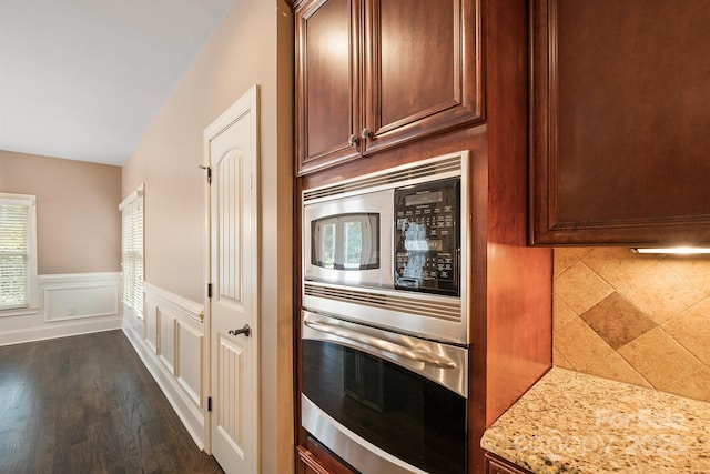 kitchen with a wainscoted wall, appliances with stainless steel finishes, dark wood-style flooring, and light stone counters