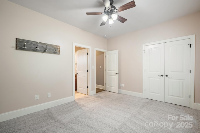 unfurnished bedroom featuring baseboards, light colored carpet, ensuite bath, ceiling fan, and a closet