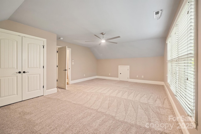 additional living space with ceiling fan, light colored carpet, visible vents, baseboards, and vaulted ceiling