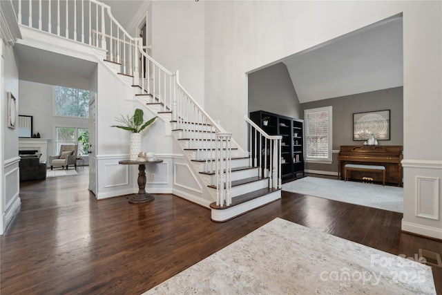 entrance foyer with dark wood finished floors, a fireplace, a decorative wall, a high ceiling, and stairs