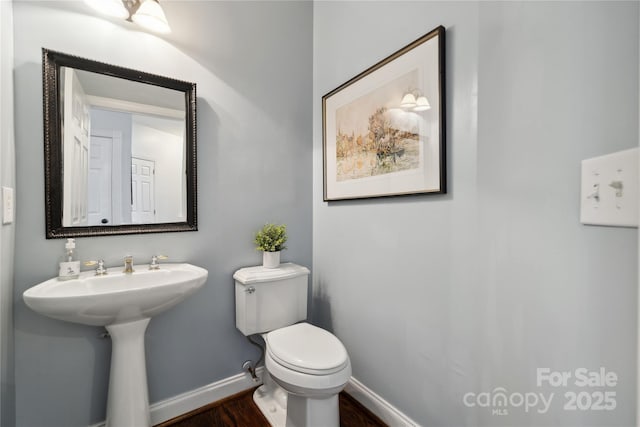 half bath with toilet, baseboards, and wood finished floors