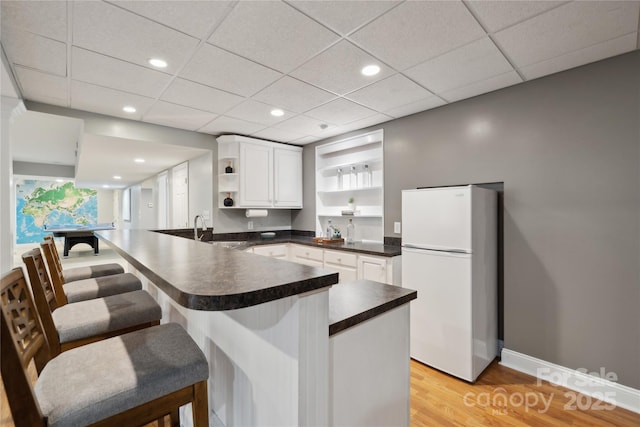 kitchen featuring dark countertops, freestanding refrigerator, a peninsula, white cabinetry, and open shelves