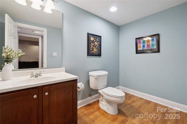 bathroom with toilet, vanity, wood finished floors, a chandelier, and baseboards