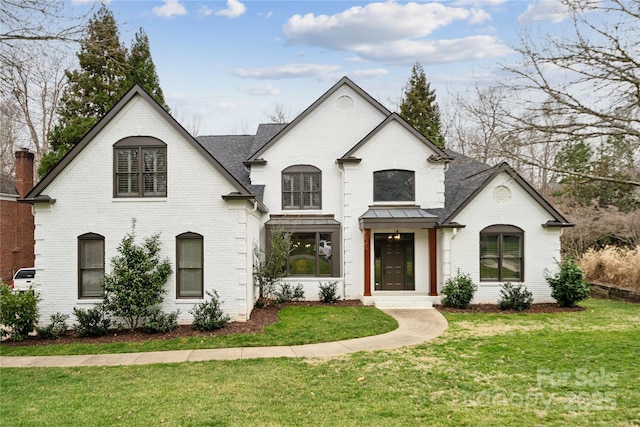 french country inspired facade with roof with shingles, brick siding, and a front lawn