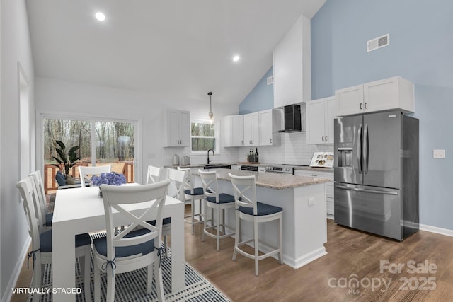 kitchen with pendant lighting, stainless steel fridge with ice dispenser, visible vents, a kitchen island, and wall chimney exhaust hood